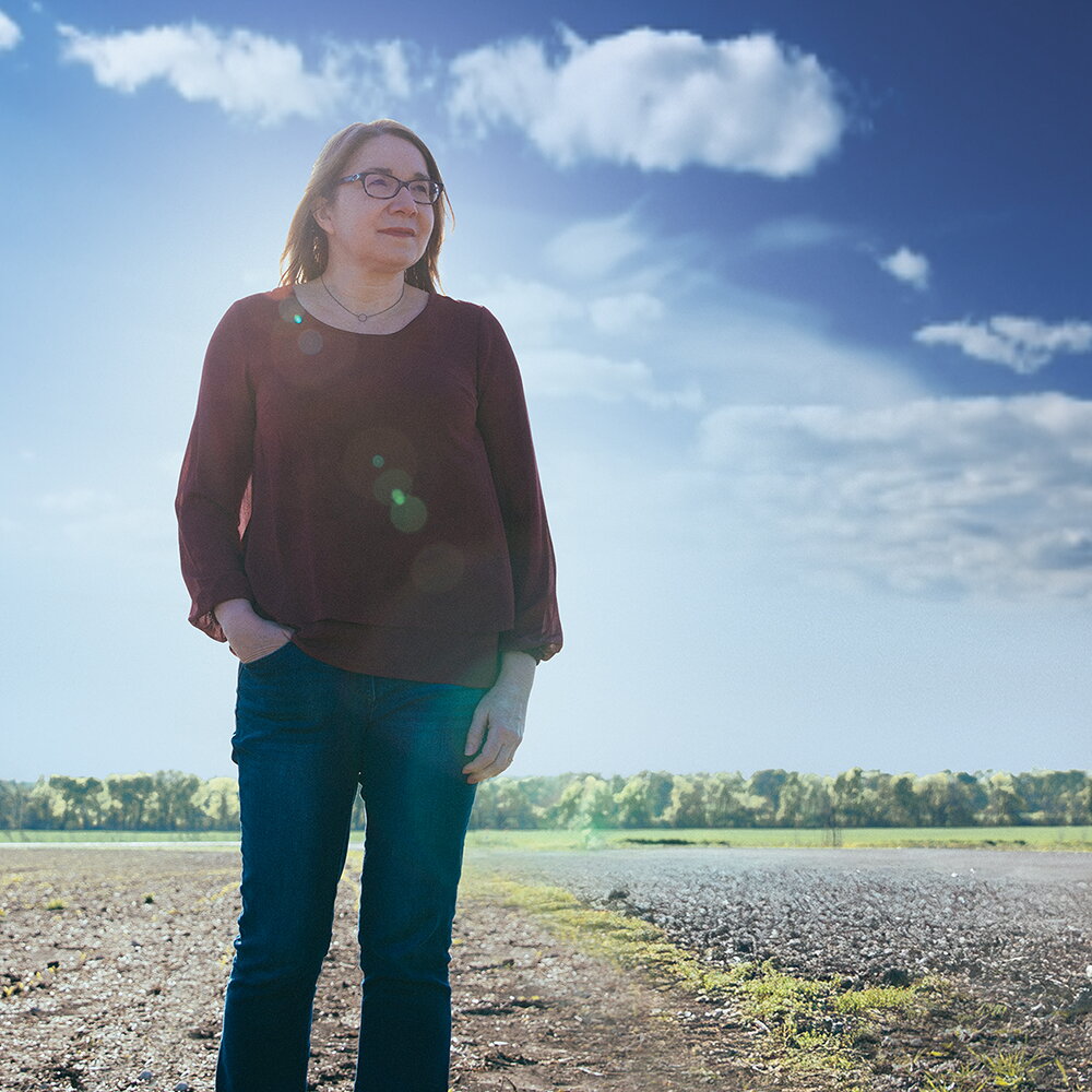 Katharine Hayhoe standing in a farm field with one hand in her pocket